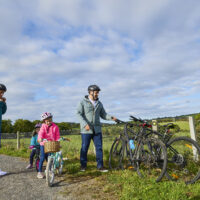 A scenic photo of Waterford Greenway in County Waterford, featuring a paved path, lush greenery, and distant hills under a clear blue sky.